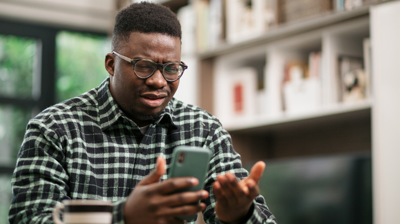 person frowning and gesturing at smartphone