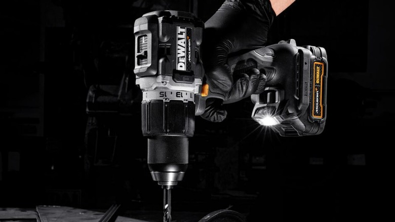 A gloved hand holding a DeWalt-McLaren drill downward.