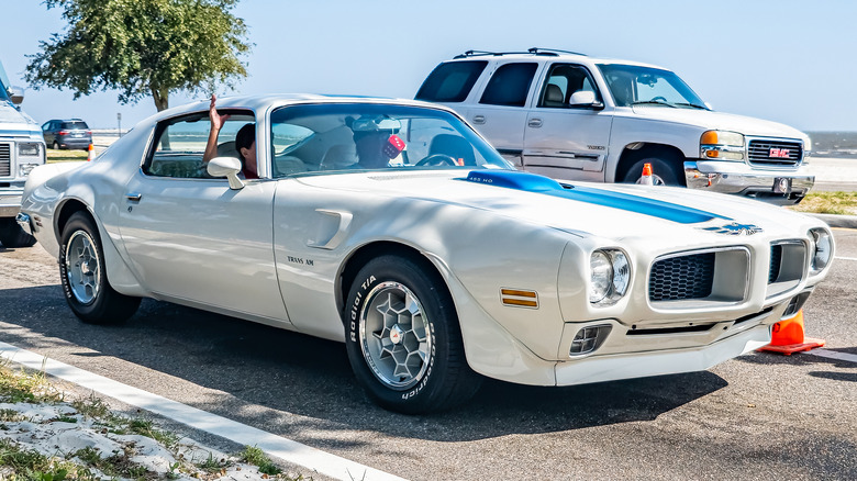 A white Pontiac Trans Am with honeycomb wheels.