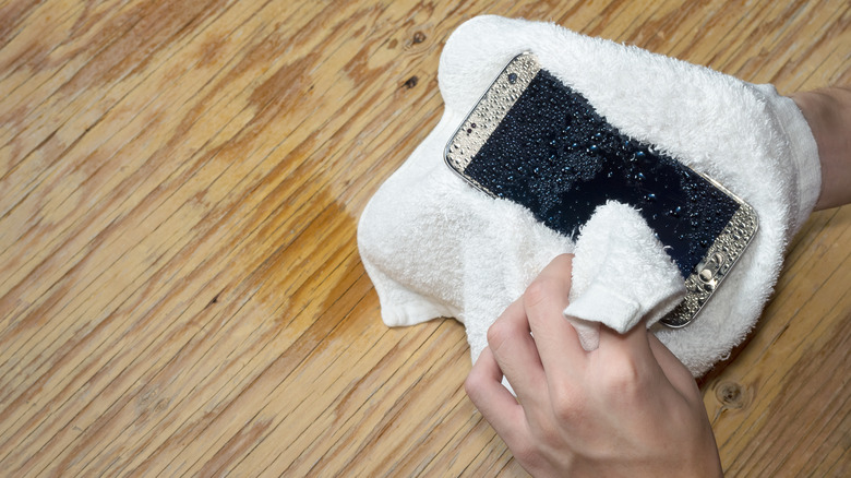 person drying a wet phone with a towel
