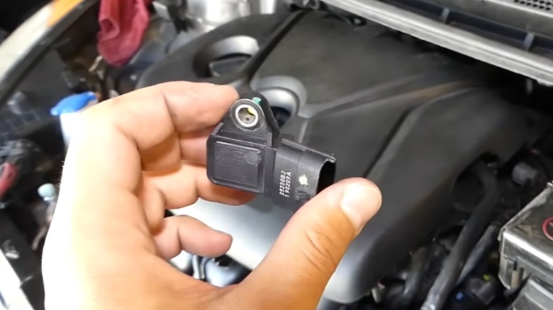 A person holding a MAP sensor in front of an engine