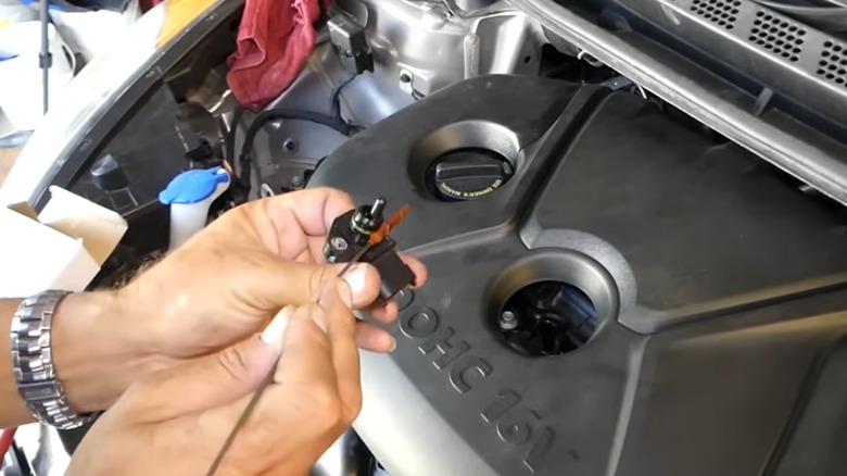 A person cleaning a MAP sensor in front of an engine bay