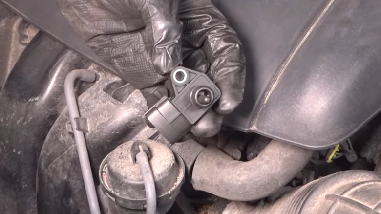 A person holding a MAP sensor in the engine bay