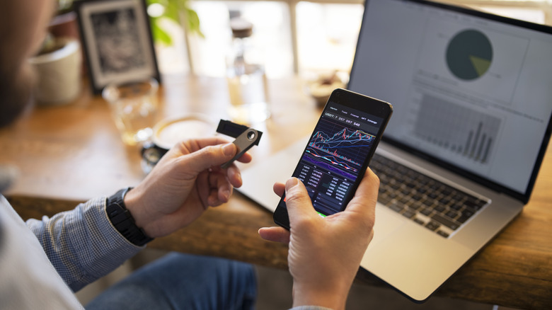 Person holds smartphone and flash drive in front of laptop