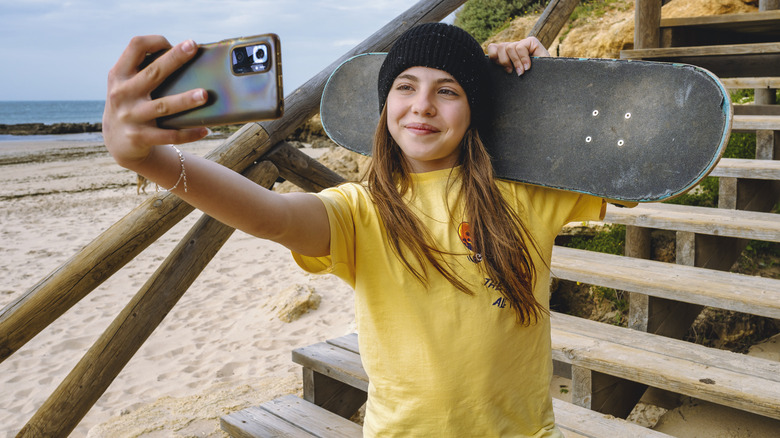 kid holding skateboard taking photo with smartphone