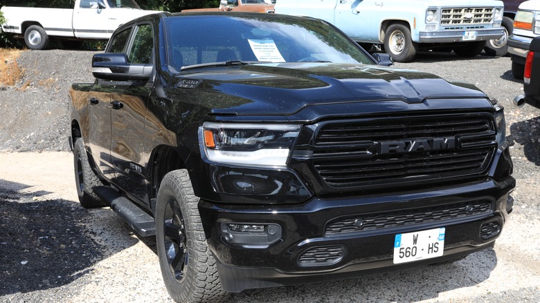 black 2021 RAM 1500 pickup parked in gravel lot with other trucks in background