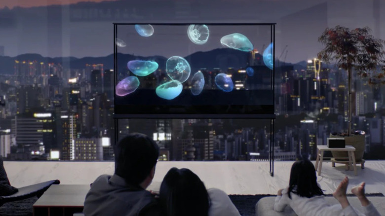 Family watching the LG OLED T in transparent mode with the cityscape showing in the background