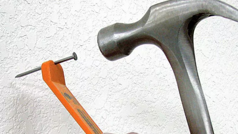 A hammer prepared to hit a nail held by a nail setter.