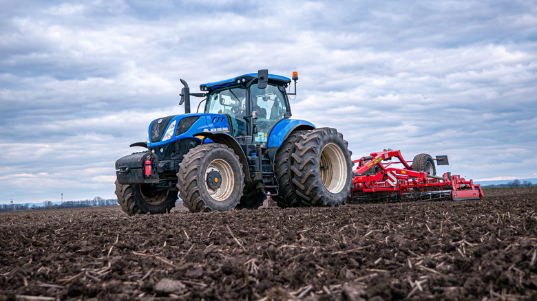 A blue New Holland tractor driving across a dirt field