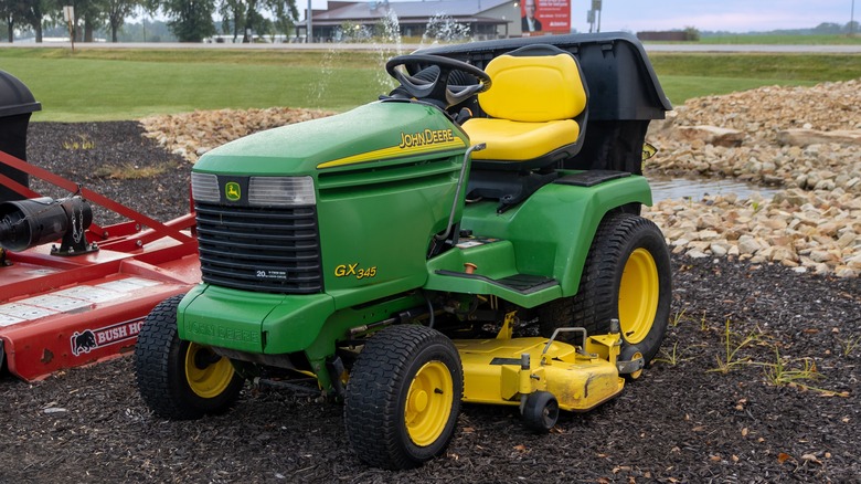 A riding John Deere lawn mower parked on mulch.