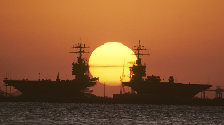 Two aircraft carriers docked with setting sun behind them