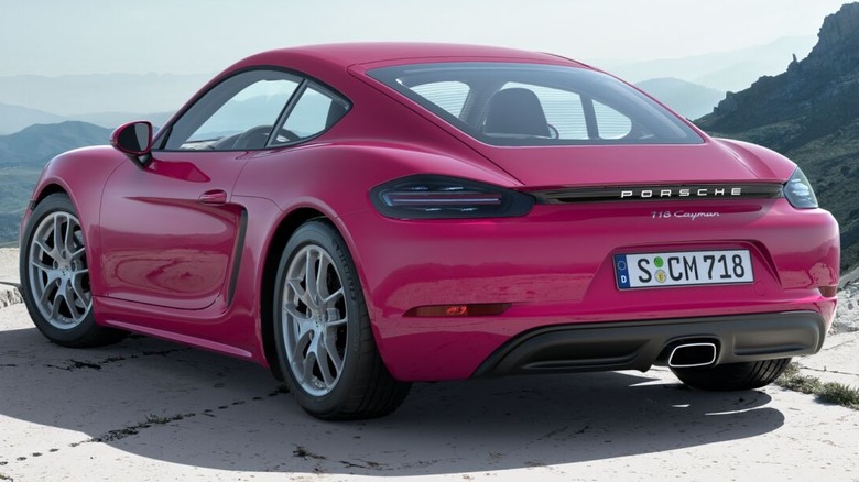 A vivid pink Porsche 718 Cayman coupe parked at a scenic overlook.