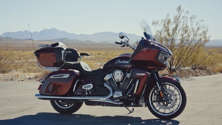 A maroon 2025 Indian Pursuit parked beside the road with hills in the background