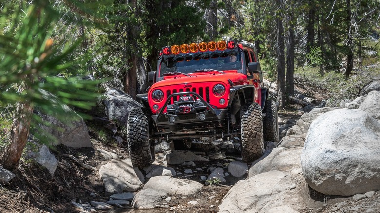 Red Jeep Wrangler Rubicon Trail traversing a rocky trail in the forest