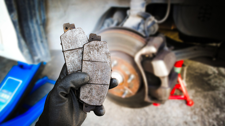 Person holding up brake pads near a car on a jack