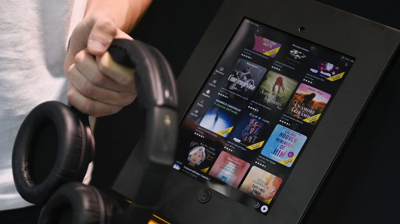 Person holding headphones in front of screen with audiobook selection