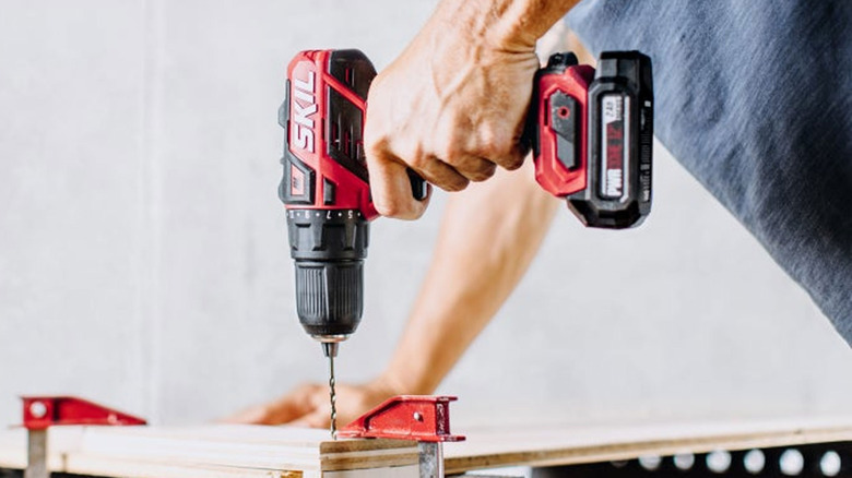 man drilling using a red and black Skil power drill