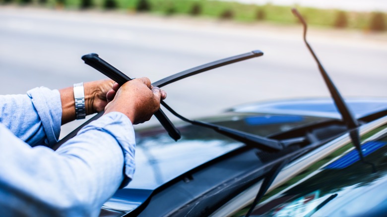 A person removing an old windshield wiper blade for replacement.