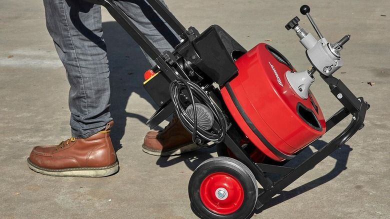 A person wheeling a Bauer drum drain auger.