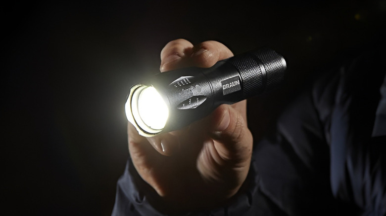 Man holding shining flashlight in darkness