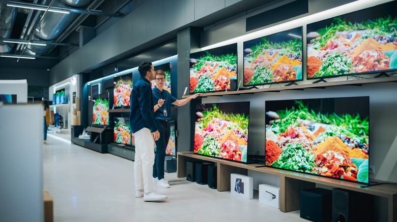 A Sales Person Talking To A Customer In Front Of Several Flat Screen TVs