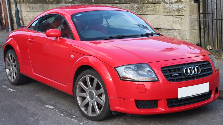 A red Audi TT parked next to a sandstone wall.