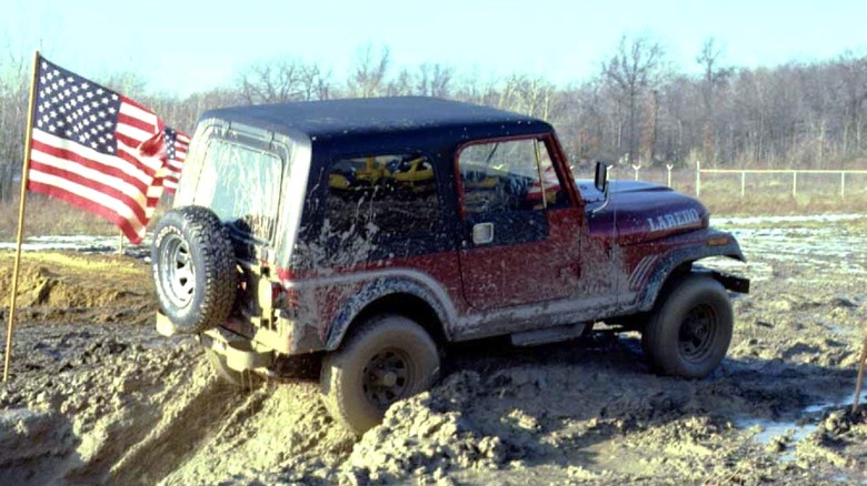 A Jeep Laredo rides through the mud with American flag standing behind it