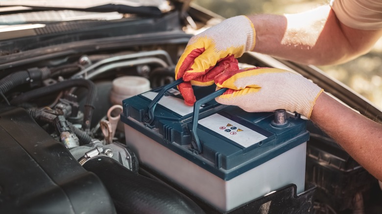 Person installing a battery inside an engine bay of an ICE vehicle