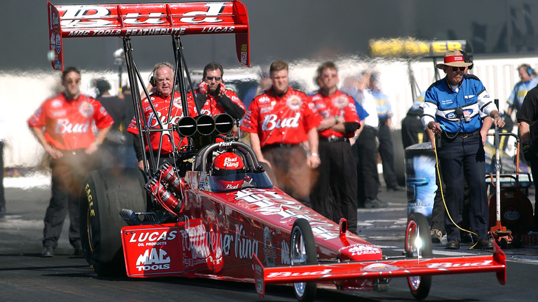 Red drag racing car on track with crew standing behind