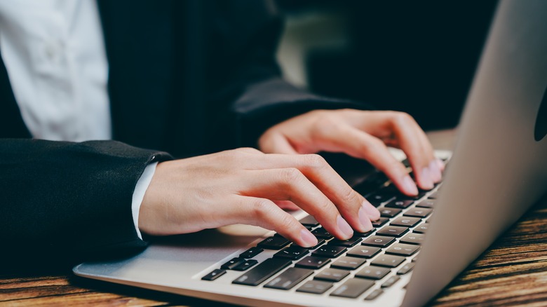 A woman has her fingers placed on the home row keys of her laptop