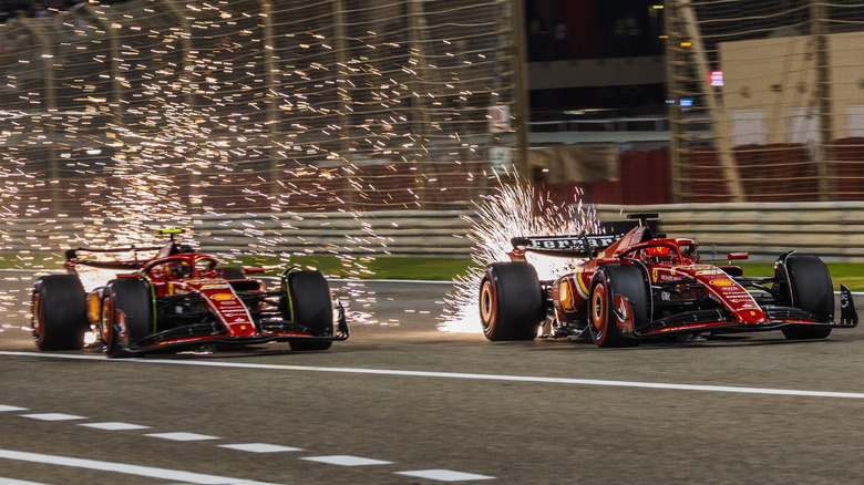 Two Ferrari F1 cars race with sparks behind them