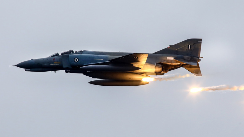 A military jet releasing flares in flight.