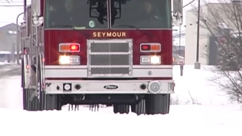 A fire truck on a snowy street with chains dangling beneath its chassis.