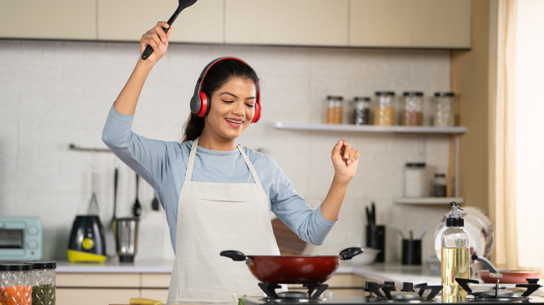 A woman wears headphones while preparing a meal in the kitchen