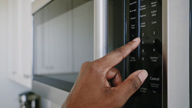 A hand touches the controls of a microwave oven