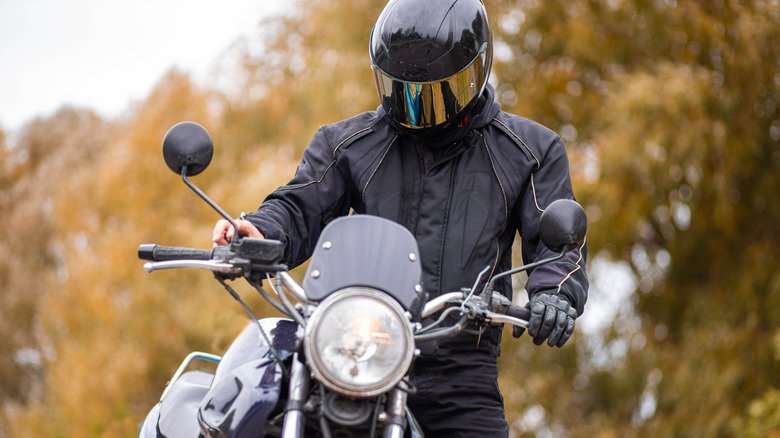 A motorcycle rider sitting outside on their bike and wearing a helmet.