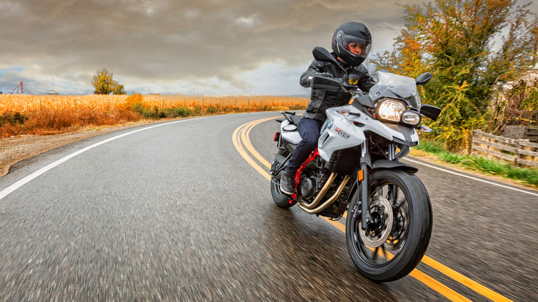 A motorcyclist is riding his bike near the center yellow line on the road.