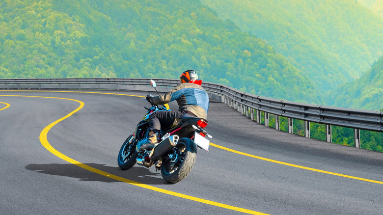 A motorcyclist is riding his bike near the center yellow line on the road with a curve ahead.