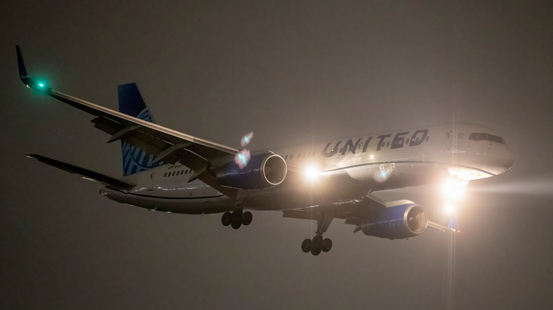 A commercial airplane with its navigation lights and headlights on, preparing to land on the runway