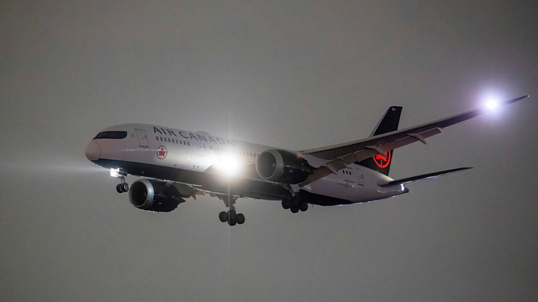 A commercial airplane with its headlights on, preparing to land on the runway