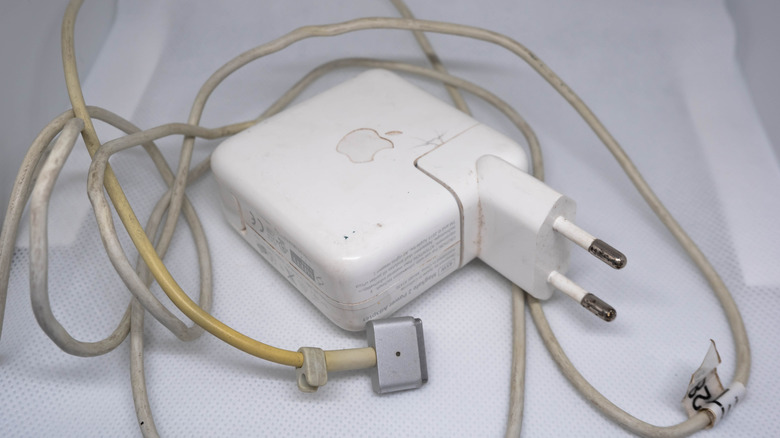 A dirty, yellowing MacBook charger jumbled up on a white surface.