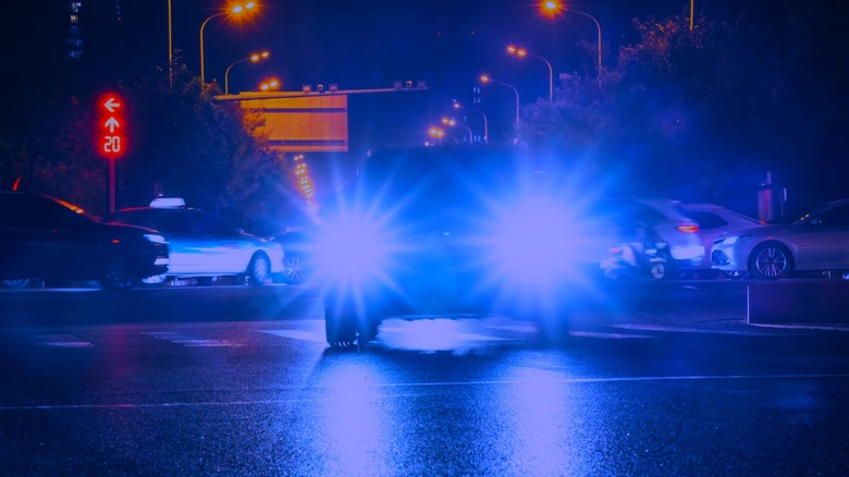 Car with blue headlights driving down street at night