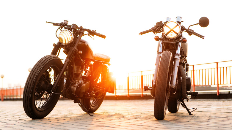 two Cafe Racers backlit by the sun With X On Headlight of one of them