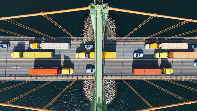 Several large trucks crossing a bridge with a few sedans