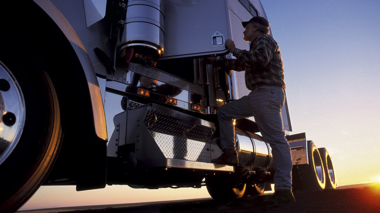 A man climbing into a semi-truck at sunset.