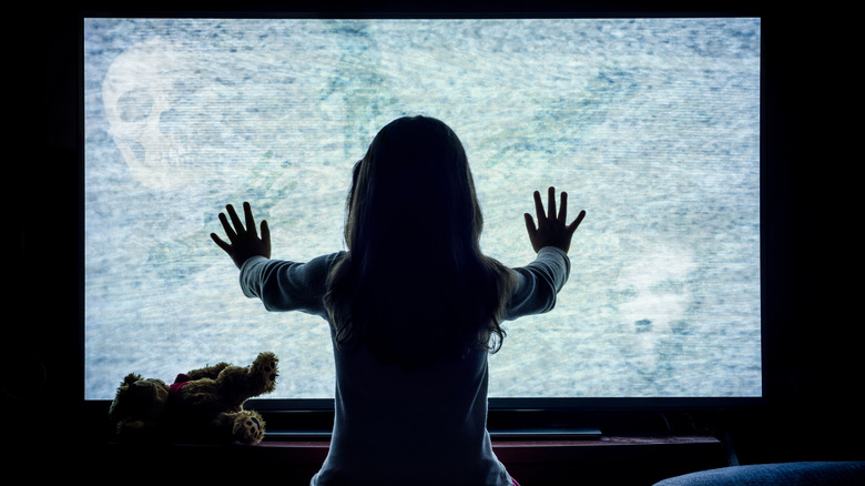 A girl presses her hands against a possessed television screen