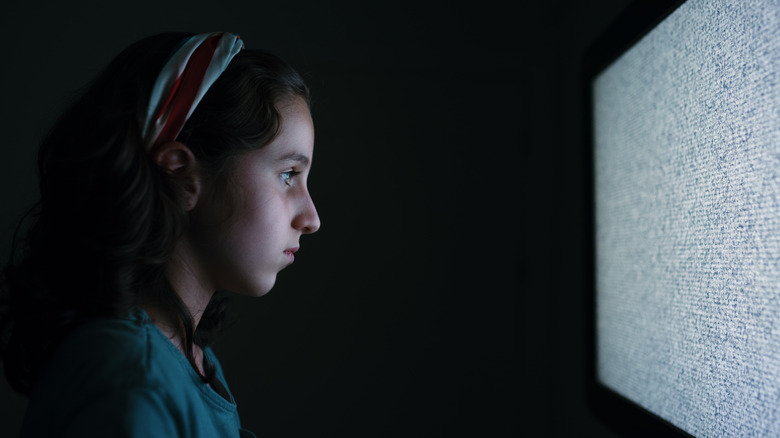 A girl worryingly stares at a static television screen at night