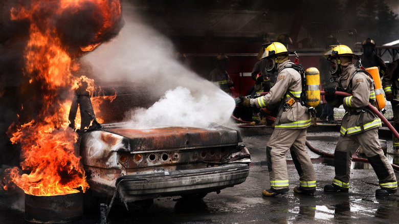 Firefighters extinguishing the flames on a burning vehicle.