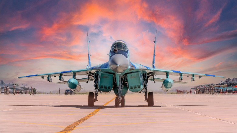 A MiG-29 on tarmac with red and orange clouds overhead.