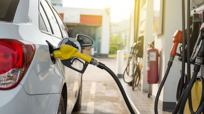 Gas being pumped at a station with a white car in the picture